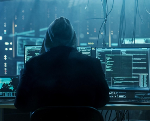 Image of a hooded person remotely hacking into systems.