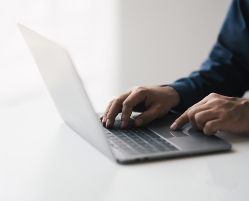 Cropped shot of young businessman hand typing on laptop computer while working in white modern office room